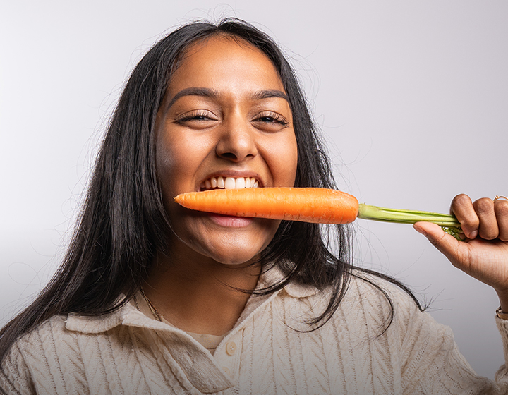 Frau beißt lachend mit strahlenden weißen Zähnen in eine Karotte