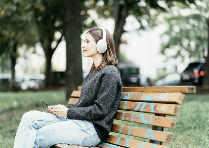 Frau mit Kopfhörern sitzt auf einer Bank im Park.