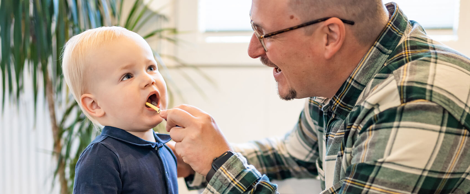 Junger Mann putzt die Zähne eines Kleinkindes.