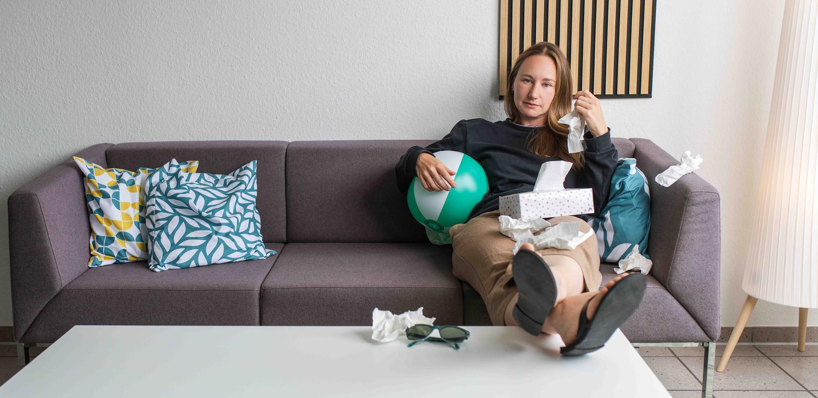 Frau sitzt auf Couch und putzt sich die Nase