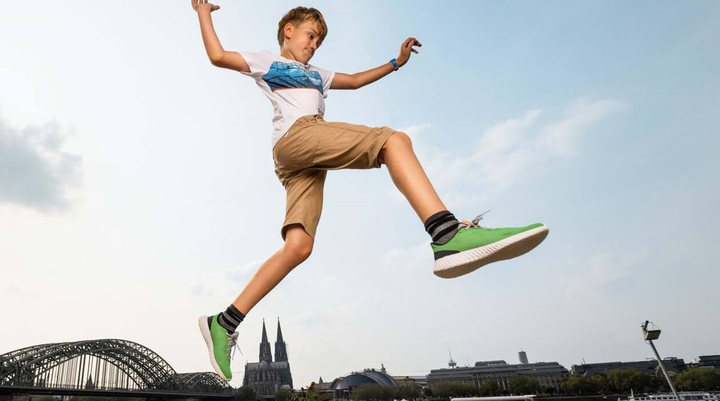 Ein Junge mit grünen Turnschuhen springt vor dem Kölner Dom.
