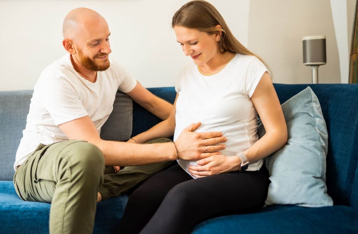 Mann legt die Hand auf den Babybauch seiner Frau.