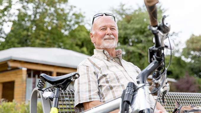 Älterer Mann sitzt auf einer Bank, vor ihm ein Fahrrad