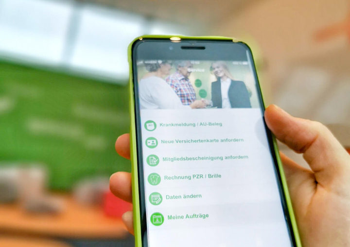 Hand hält Handy mit Bergische Krankenkasse App.