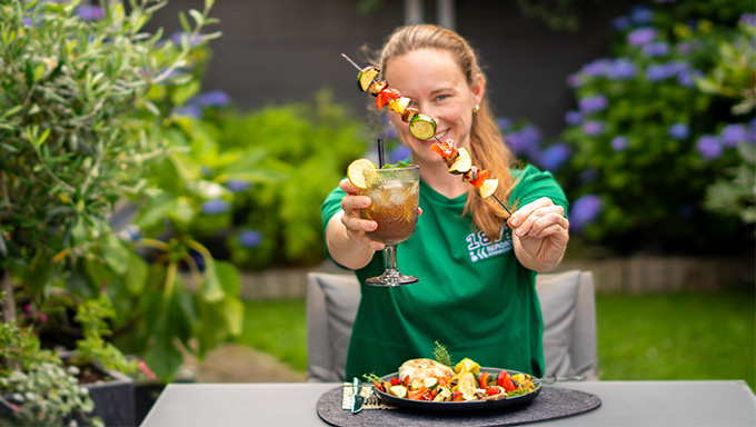 Frau zeigt Essensspieß und Cocktail in die Kamera