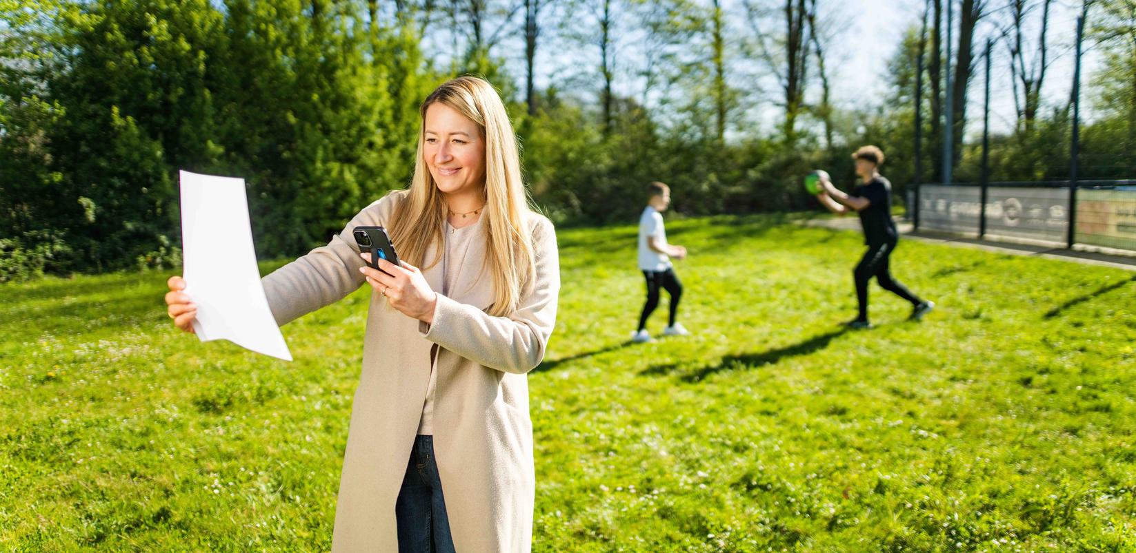 Frau fotografiert Rechnung während ihre Kinder im Hintergrund auf der Wiese Sport machen