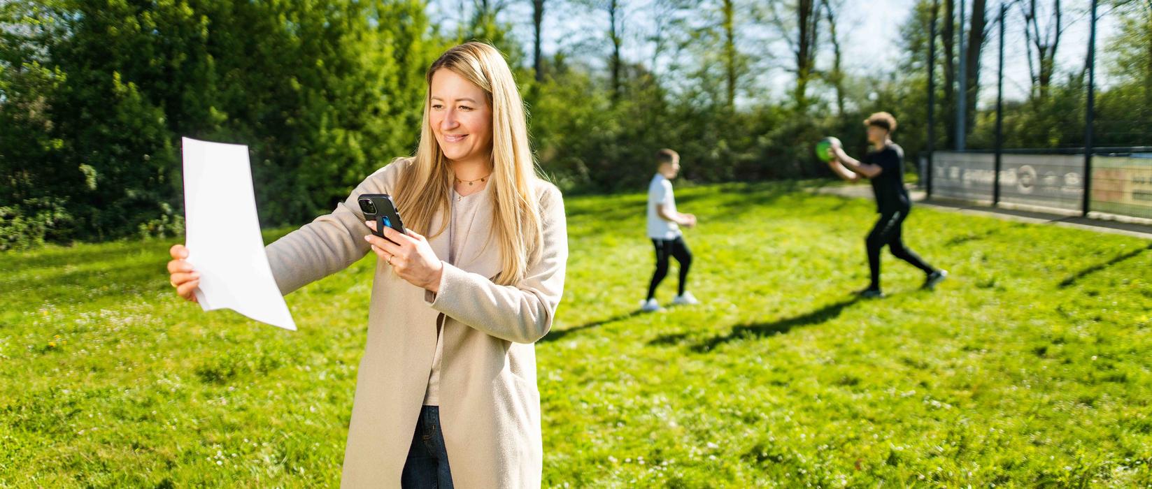 Mutter fotografiert eine Rechnung während die Kinder im Hintergrund Sport machen