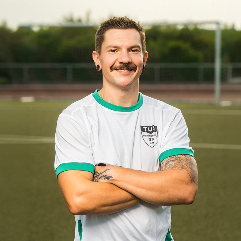 Fußballspieler mit verschränkten Armen der in die Kamer lächelt