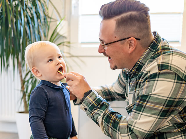 Junger Mann putzt Zähne eines Kleinkindes.